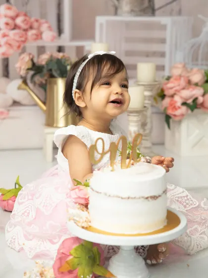 A radiant smile from the birthday princess. Dressed in a beautiful lace gown, she is surrounded by a soft, romantic floral setup, perfect for her first birthday photos.