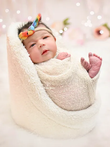 This baby girl is awake and looking at the camera, wrapped in a cozy white blanket with a rainbow bow adding a pop of color.