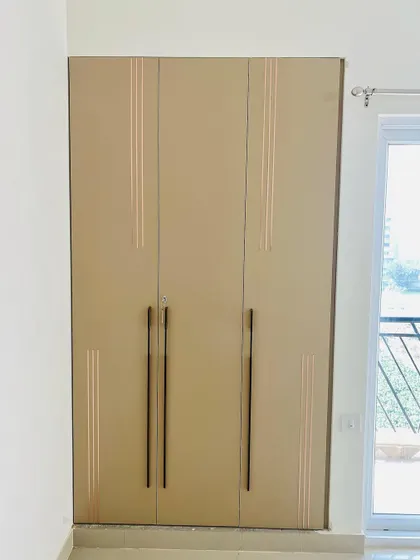 A three-door wardrobe with elegant rose gold inlay details and long, modern handles.
