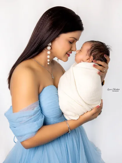 A tender moment between a mother in a beautiful blue dress and her newborn baby. The simple white background keeps the focus on their connection.