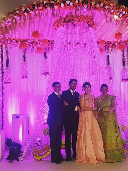 A happy family portrait on the reception stage we designed. The backdrop features cascading floral arrangements and crystal strings, all beautifully illuminated with pink uplighting.