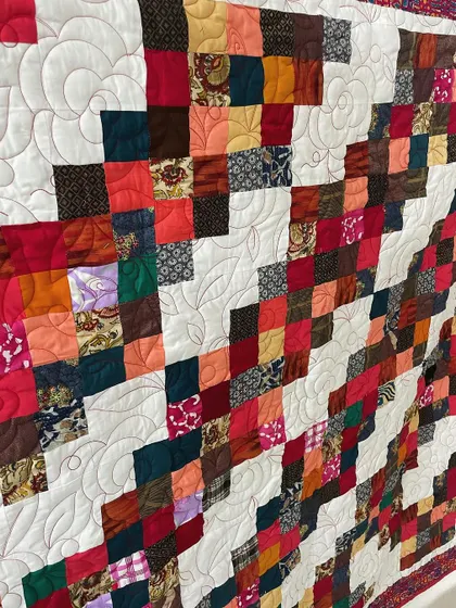 A detail shot of a scrappy quilt, with a floral quilting pattern on the white background.