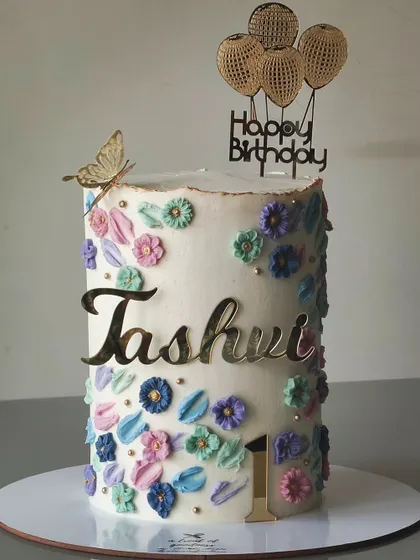 A closer look at the tall floral birthday cake. The buttercream flowers are piped in soft pastel shades and accented with small gold pearls for a delicate and pretty finish.