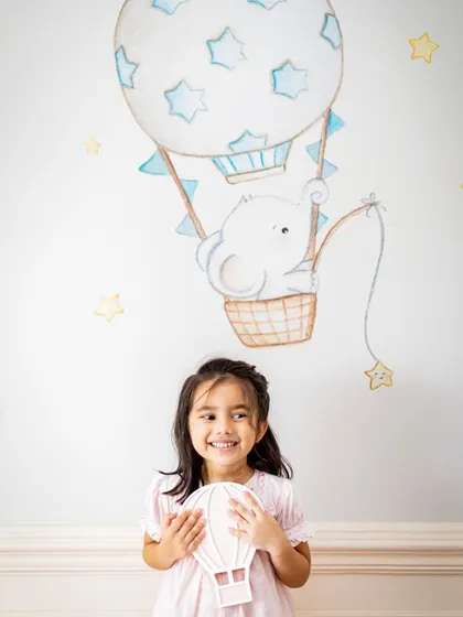 Sometimes the simplest props can spark the most imagination. This little girl poses in front of a hot air balloon wall mural in her room, creating a sweet and whimsical portrait.