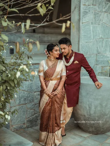 A portrait of poise and connection. The groom's rich maroon sherwani beautifully complements the bride's earthy-toned saree, captured at the elegant Amitarasa venue.