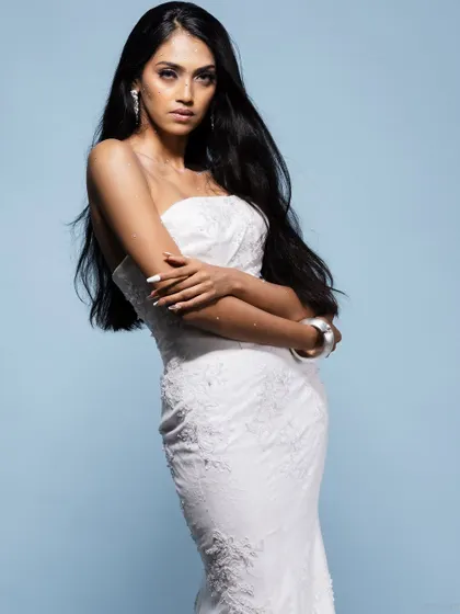 A model posing in a form-fitting white gown against a blue backdrop, perfect for a Christian bridal or evening wear lookbook.