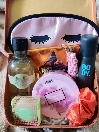 A cozy and compact hamper for your sister or friend. This gift, packed in a reusable tin box, includes an eye mask, body spray, perfume, a Nykaa compact, and a Hershey's chocolate bar.