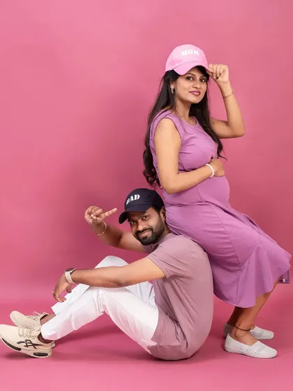 A cool and casual couple's portrait with matching "Mom" and "Dad" caps. This fun pose against a pink background shows off their playful personalities.