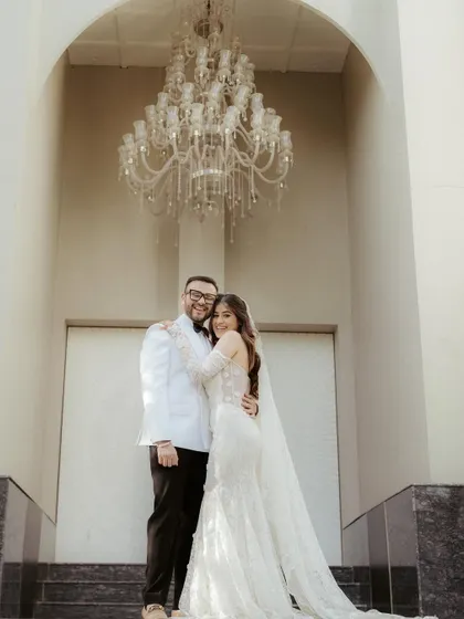 A grand portrait of the couple in their white wedding attire, standing beneath a magnificent chandelier, exuding classic elegance.