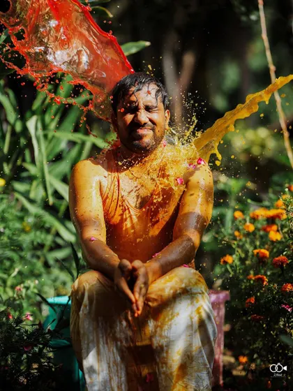 An action shot of the groom being splashed with red and yellow water, capturing the peak of the fun.