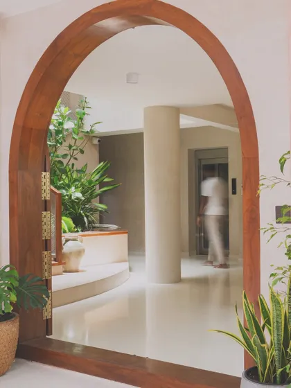 The entryway of this home is designed around a central staircase and a planter bed, reminiscent of a traditional courtyard. The wooden archway frames the view, creating a layered and welcoming first impression.