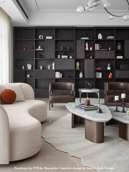 A custom floor-to-ceiling bookshelf becomes the architectural anchor in this living room. The dark wood of the cabinetry is balanced by a light, curved sofa and leather armchairs. The organic shapes of the tables and rug soften the geometry of the space.