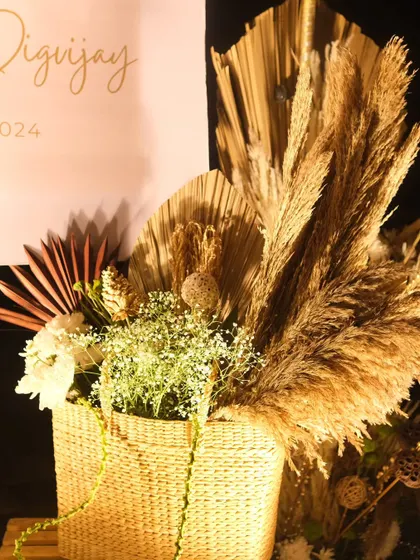 A detailed shot of a boho floral arrangement in a wicker basket. This piece combines dried pampas grass, palm leaves, and delicate white flowers for a beautifully textured and natural look.