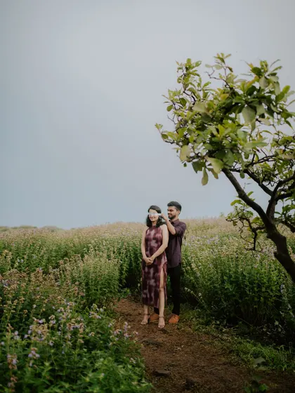 A creative portrait of a couple under a tree in a field, showcasing a candid and natural interaction.