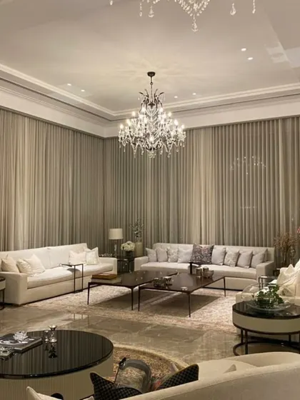 A grand and luxurious living room with classic furniture, a crystal chandelier, and floor-to-ceiling curtains, showcasing our work in a more opulent style.