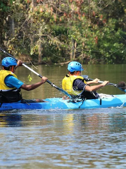 Guests in a blue kayak paddle along the tree-lined riverbank. The calm water and lush surroundings make for a truly picturesque journey.