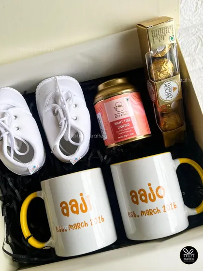 The complete flat-lay of our grandparents' announcement box, showcasing the personalized mugs, baby shoes, tea, and chocolates nestled in the gift box.