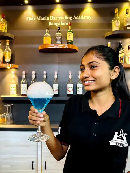 A happy bartender presenting her latest creation, a blue cocktail topped with a large, smoke-filled bubble.