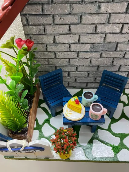A detailed shot of a coffee and cake scene on another custom diorama. The tiny mugs and slice of cake are all part of the story we create together for your nameplate.
