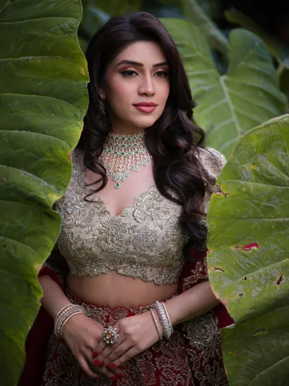 A creative shot of Mahima peeking through large tropical leaves. Her makeup looks fresh and glowing, even in the natural outdoor light.