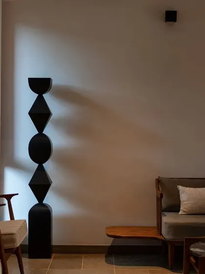 A play of light and shadow on a minimalist interior, highlighting a geometric black sculpture. The image captures the artistic and contemplative mood of the "In The Hills" sanctuary.