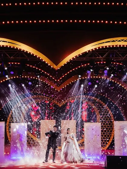 The couple takes the stage for their performance, surrounded by confetti and the dazzling lights of the heart-themed backdrop.