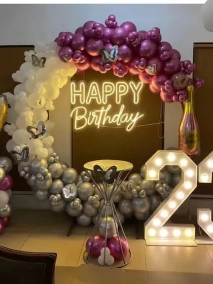 A 23rd birthday party with a half-moon balloon arch in white, silver, and magenta. The decor includes marquee numbers and creative balloon sculptures shaped like a champagne bottle and glass.