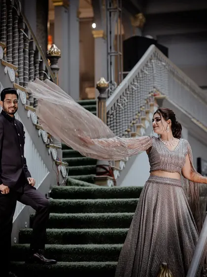 A fashionable couple poses on a grand staircase, the bride's flowing lehenga creating a dramatic and beautiful effect.