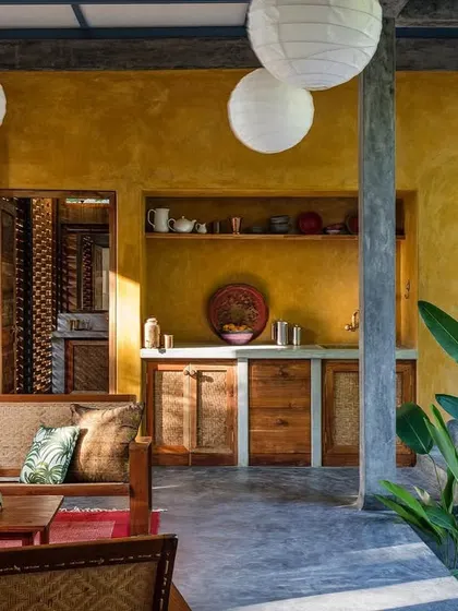 The living area of a private villa at Jalakara, which opens completely to a plunge pool. The design uses a palette of polished concrete, warm wood, and yellow oxide walls, creating a space that is both modern and tropical.