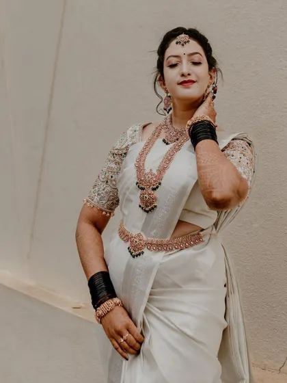 A full-length portrait of a South Indian bride in an elegant white saree, adorned with traditional jewelry. This shot showcases her complete bridal look with grace.