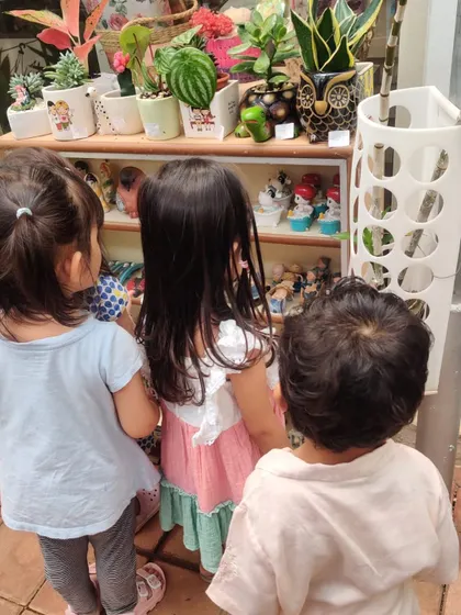 Three children curiously examine decorative garden gnomes and colorful pots at the nursery.