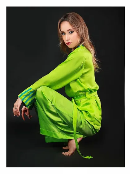 A lookbook image for a luxury sleepwear or loungewear brand. The vibrant green silk outfit is showcased against a clean black background to make the color and texture pop.