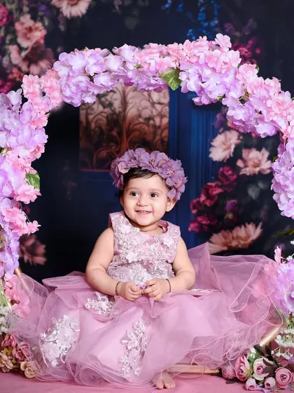 For this pre-birthday shoot, we created a dreamy floral wonderland. This little one is sitting on a beautiful swing adorned with pink and purple flowers, creating a magical portrait.