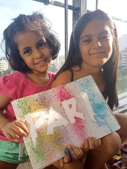 Two sisters proudly display their spray-paint artwork created at home. Our distance learning program encourages children to explore different art mediums and work collaboratively.