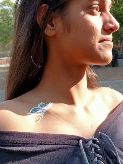 A temporary tattoo of a Krishna-inspired flute and peacock feather, placed elegantly on the collarbone.