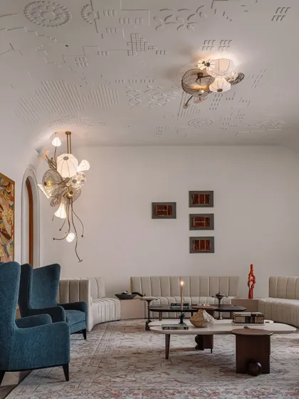Another view of the formal living room, showcasing the interplay of textures and forms. The deep blue chairs provide a pop of color against the neutral palette, while the custom lighting by Olie Lighting acts as jewelry for the ceiling.