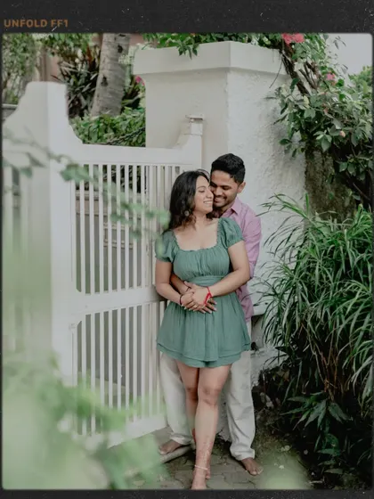 A stylish, film-noir inspired shot of the couple against a white gate, framed by dark greenery.