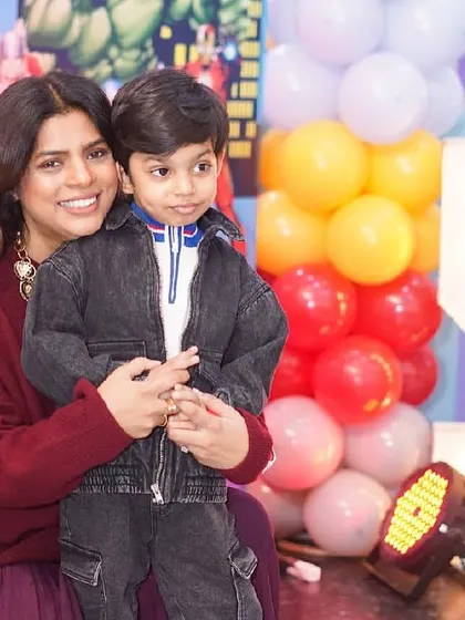 A mother holds her son, the birthday boy, for a lovely photo in front of the party decorations.
