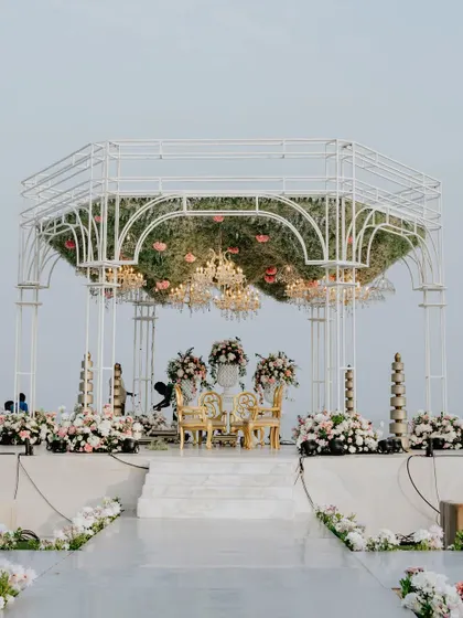 A full view of the seaside mandap, showing the elegant white structure, the lush floral arrangements in pastel hues, and the pristine white aisle leading to the ceremony space.