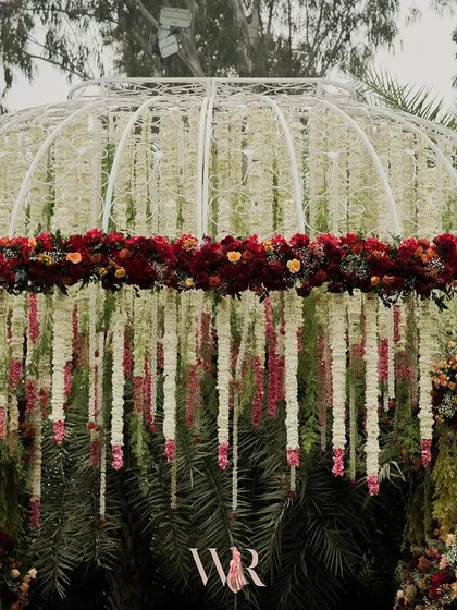 A close-up of the dome-shaped Vedi, showing the intricate layers of white floral strings accented with deep red blooms. This design is a modern take on the traditional phoolon ki chadar.