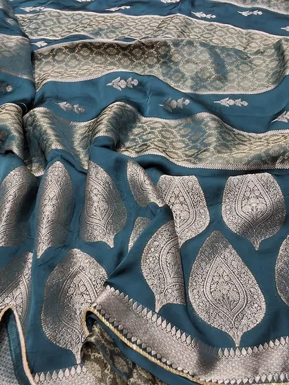 The beautiful drape of a teal green soft silk saree with intricate silver zari work. This fabric is known for its softness and sheen, making it both comfortable and glamorous.