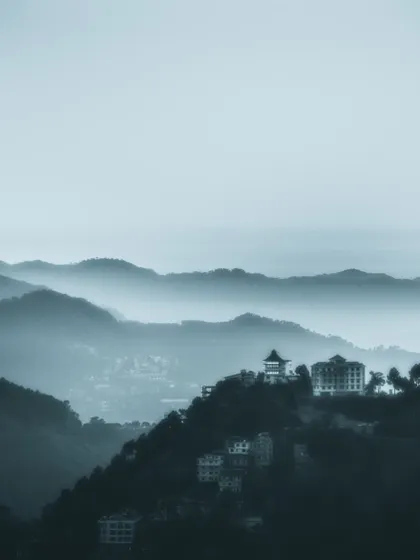 a distant building perched on a misty mountain range. this photo plays with atmospheric perspective, creating a sense of scale and distance.