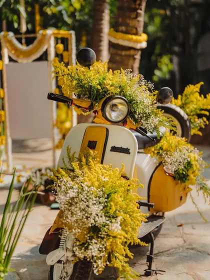 A quirky and fun decor element for the Haldi ceremony. A vintage scooter is adorned with bright yellow flowers, creating a perfect photo opportunity for guests.