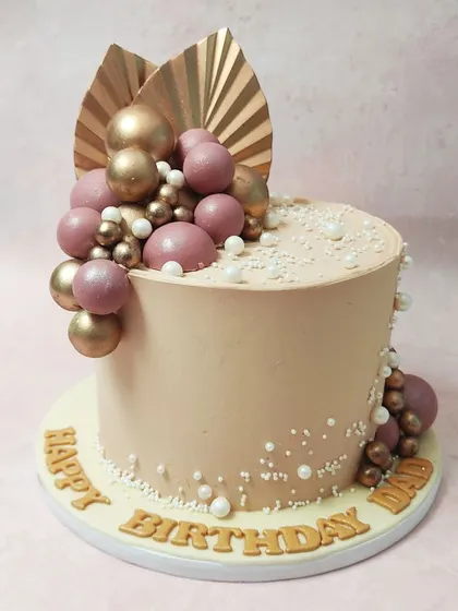 We embrace modern, elegant trends with this beautiful bohemian cake. A soft peach-colored tier is decorated with cascading pearls and clusters of mauve and gold spheres, topped with dried palm leaves for a chic and sophisticated birthday design.
