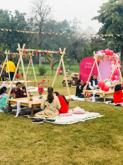 A wide shot of a pink-themed picnic party, with guests enjoying the unique low-seating arrangement under teepee-style canopies.