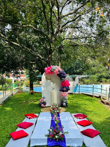 An outdoor bachelorette party by the pool. We set up a picnic-style dining area and a modern arched backdrop with a balloon garland in shades of pink, grey, and purple.