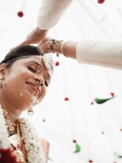 A close-up of the bride's blissful expression as she is showered with blessed rice. The high-key lighting and tight crop emphasize her happiness.