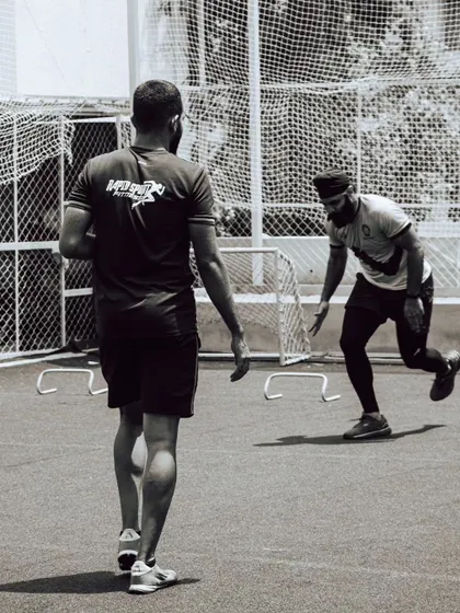 A coach observes an athlete performing hurdle drills. This black-and-white shot captures the focus and dedication present in our training sessions, where every movement is analyzed for improvement.