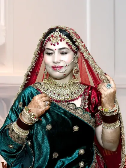 A classic bridal portrait in a stunning green and red velvet lehenga. The soft lighting and the bride's gentle pose create a timeless and elegant look.