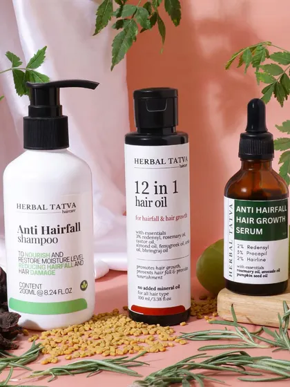A group shot of an anti hairfall range, styled with the natural ingredients mentioned in the products. This composition highlights the herbal and natural formulation of the shampoo, oil, and serum.